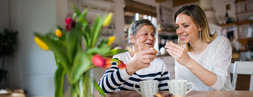 Image of middle aged woman and senior female friend having snack with their warm beverages